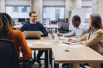 Professional team engaged in a collaborative meeting, discussing ideas in a contemporary office environment with laptops and documents