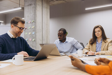 Diverse group of professionals engaging in a collaborative meeting at a modern office table, using laptops and digital devices for work