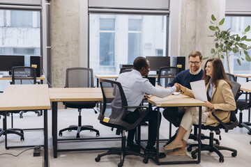 Diverse professionals discussing project details during collaborative meeting, working together in modern office workspace