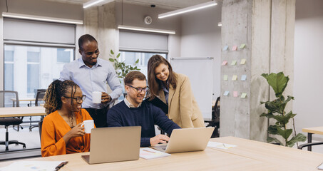 Professional team collaborating, sharing innovative ideas with laptops in contemporary workplace, representing diverse workforce dynamics