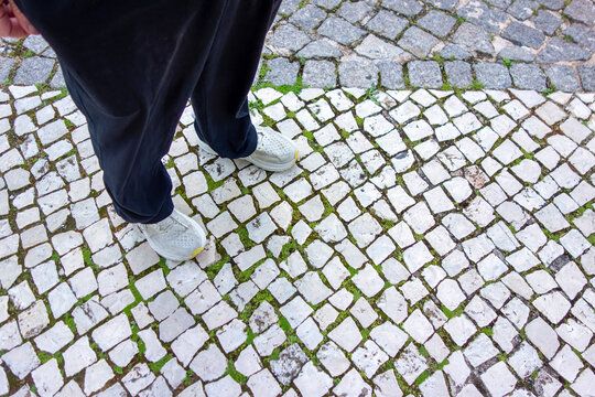A man's feet in sneakers walking on ancient mosaic cobblestone pavement travel tourism background with copy space Europe Algarve Portugal