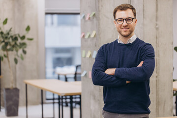 Fototapeta premium Professional businessman wearing glasses standing confidently near sleek workspace, illuminated by bright ambient lighting