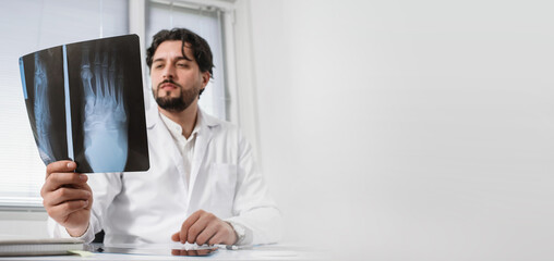 Doctor surgeon traumatologist looks at an X-ray of the foot. fracture, arthrosis, arthritis, joint deformation, dysplasia, meniscus injury. orthopedist specialist consultation banner copy space