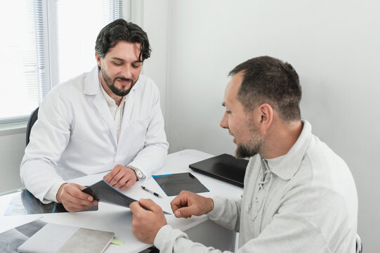 Doctor surgeon traumatologist looks at an X-ray with male petient. fracture, arthrosis, arthritis, joint deformation, dysplasia, meniscus injury. orthopedist specialist consultation