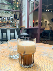 Glass of iced espresso with straw on wooden table in modern cafe