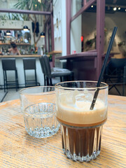 Glass of iced espresso with straw on wooden table in modern cafe