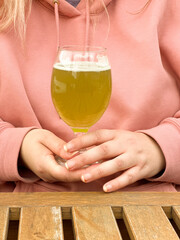 Woman in pink hoodie holding glass of matcha beer at wooden table