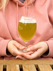 Woman in pink hoodie holding glass of matcha beer at wooden table