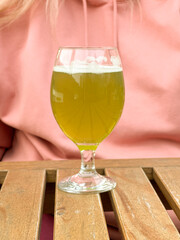 Woman in pink hoodie holding glass of matcha beer at wooden table