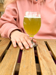 Woman in pink hoodie holding glass of matcha beer at wooden table