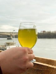 Hand holding glass of matcha beer against river view,