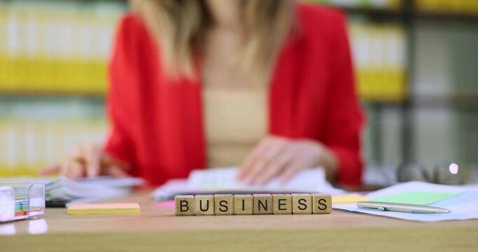 Businesswoman reviews financial documents and graphs at desk with wooden cubes having word business. Lady focuses on work in office setting