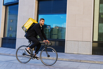 A bicycle courier rides along the street with a yellow backpack. Delivery in the city in a fast...