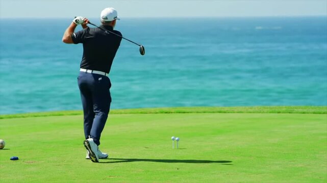 A golfer, dressed in black, walks toward the tee box on a stunning coastal golf course. The ocean sparkles in the background, creating an inviting scene for a day of play