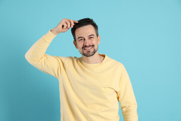 Naklejka premium Handsome man stylish his hair with comb on light blue background