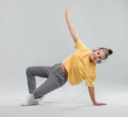 Zelfklevend Fotobehang Girl with headphones in stylish clothes dancing on light grey background © New Africa