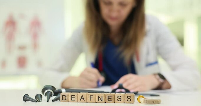 Word Deafness on wooden blocks near otoscope in hospital office. Female doctor fills medical records diagnosing hearing loss diagnostic process