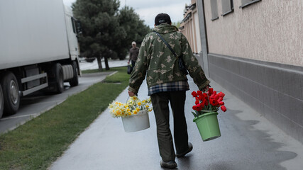 Man carrying flower buckets on a cloudy day in a city street