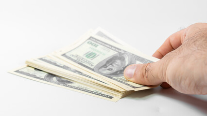 Hand holding stack of hundred dollar bills on neutral background displaying currency value and...