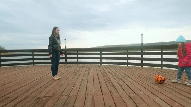 Mother and daughter at the pier near the water having fun. Mom with little girl playing a ball