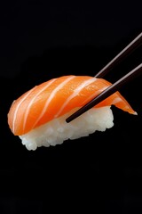 Salmon nigiri sushi held by chopsticks on black background
