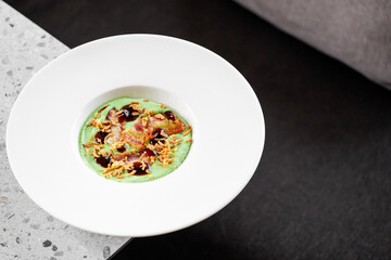 A gourmet dish featuring green pea puree, crispy bacon, fried onions, and balsamic glaze, elegantly...