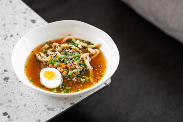 bowl of steaming ramen with noodles, boiled egg, fresh vegetables, and sesame seeds, served on a speckled countertop. Vibrant colors and rich textures create an appetizing presentation.