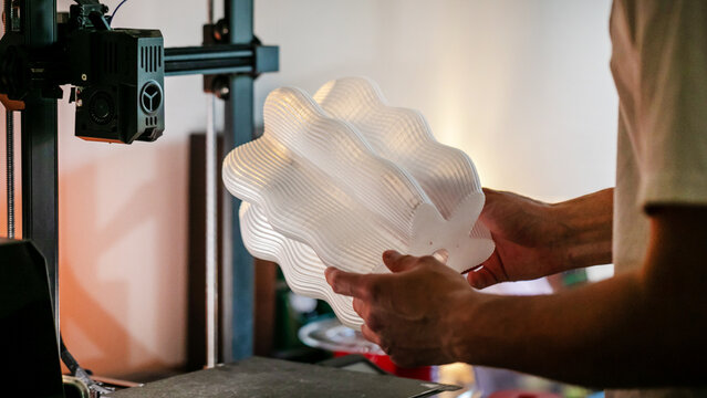 Crafting a translucent fan-like sculpture, an innovative Asian male explores modern alchemy during Makers Faire; 3D printer, 3D printing