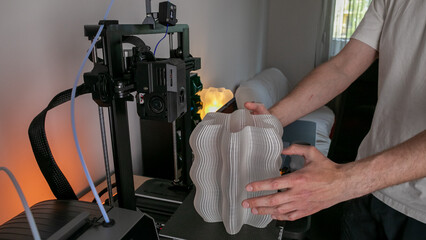 A Caucasian male marvels at a beach-inspired, sculptural vase emerging from a modern contraption,...