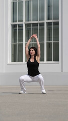 A woman performs a deep squat with her arms extended overhead, engaging core and leg muscles. This...