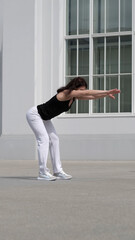 A woman performs a forward stretch, engaging her core and back muscles in an outdoor workout. The...