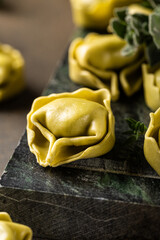 Close up view of raw tortellini filled with ricotta and spinach, placed on a dark green textured board, garnished with fresh herbs for a rustic presentation