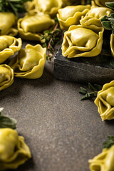 Fresh uncooked tortellini pasta with ricotta and spinach on a dark green textured board, garnished with fresh herbs for a rustic presentation. Healthy food background with copy space
