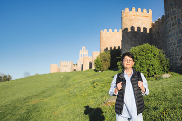 Senior tourist with a backpack is enjoying a sunny day exploring the historic walls of avila, a unesco world heritage site in spain, representing active seniors and cultural tourism