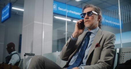International Airport Terminal: Confident Businessman Talking on Mobile Phone, Sitting in Departure...