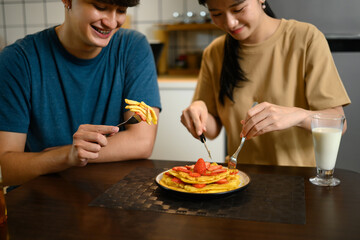 Young couple enjoying a breakfast together with pancakes and a glass of milk in home kitchen