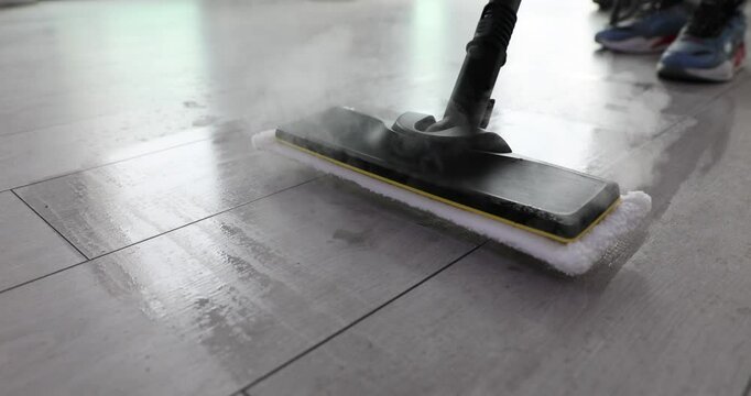 Cleaning service worker washes tiled floor with steam mop in office. Vapor cleaning and disinfection of parquet with domestic equipment at home