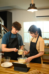 Cheerful young couple preparing breakfast pancakes in cozy home kitchen
