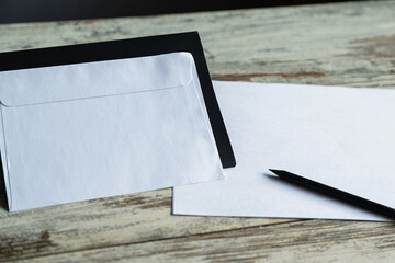 A white envelope on a black stand next to paper and a pencil is a symbol of official correspondence and business communications. For illustrating business processes, mailings, and stationery.