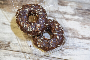 Two appetizing doughnuts with chocolate glaze in a plastic container on a white table, close-up.