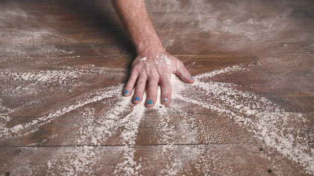 A close-up of a hand slamming down or brushing through a large cloud of white powder on a wooden surface, creating a dramatic burst or explosion of powder outward from the center.