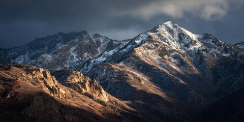 Fototapeta premium Dramatic Snow-Capped Mountain Peaks Under Cloudy Sky With Golden Light in Valley Below