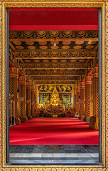 A view through the beautifully carved golden temple door frame shows a large Buddha statue inside a beautifully decorated chapel at Wat Phan On Temple, a popular landmark for tourists in Chiang Mai