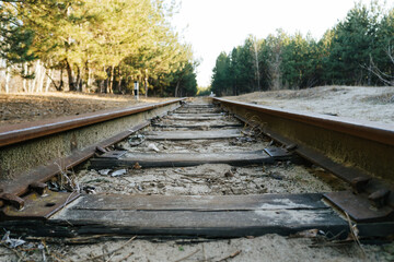 Close-up of old sleepers and narrow-gauge railway tracks stretching into the distance through a...