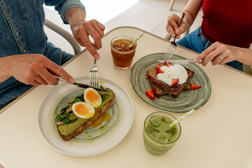 Hands of couple using cutlery, eating healthy avocado toast and french toast with strawberries and ice cream for breakfast
