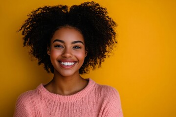 A woman with curly hair is smiling and wearing a pink sweater