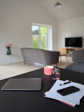 Close-up of a closed laptop computer, paperwork, pen, mobile phone and drinks on a dining room table