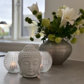 Close-up of a Buddha head ornament on a kitchen worktop with a bouquet of flowers in a vase and two tea light holders with lit candles