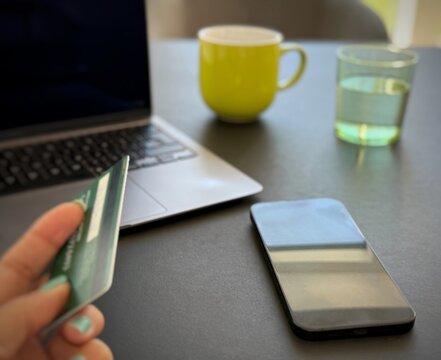 Close-up of a woman sitting in front of a computer with a blank screen holding a credit card