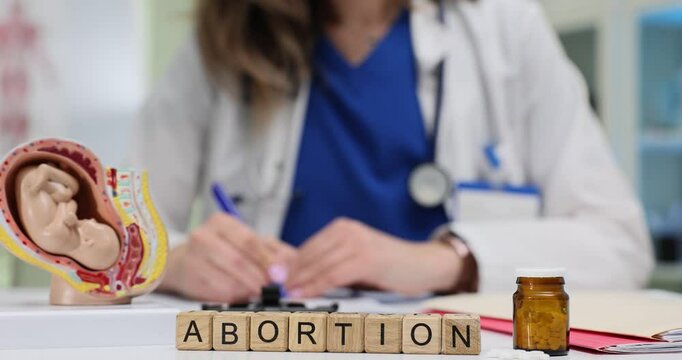 Female physician documents Abortion prescription near fetus anatomical model and pills. Reproductive healthcare medical decision making process